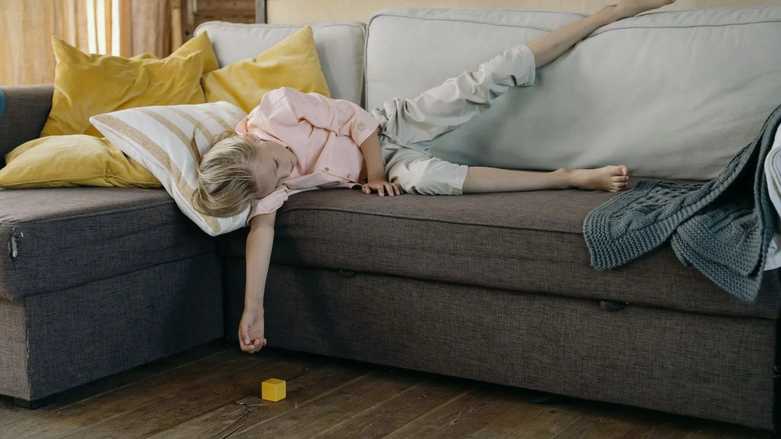A child lying on a sofa under a blanket with one arm hanging down