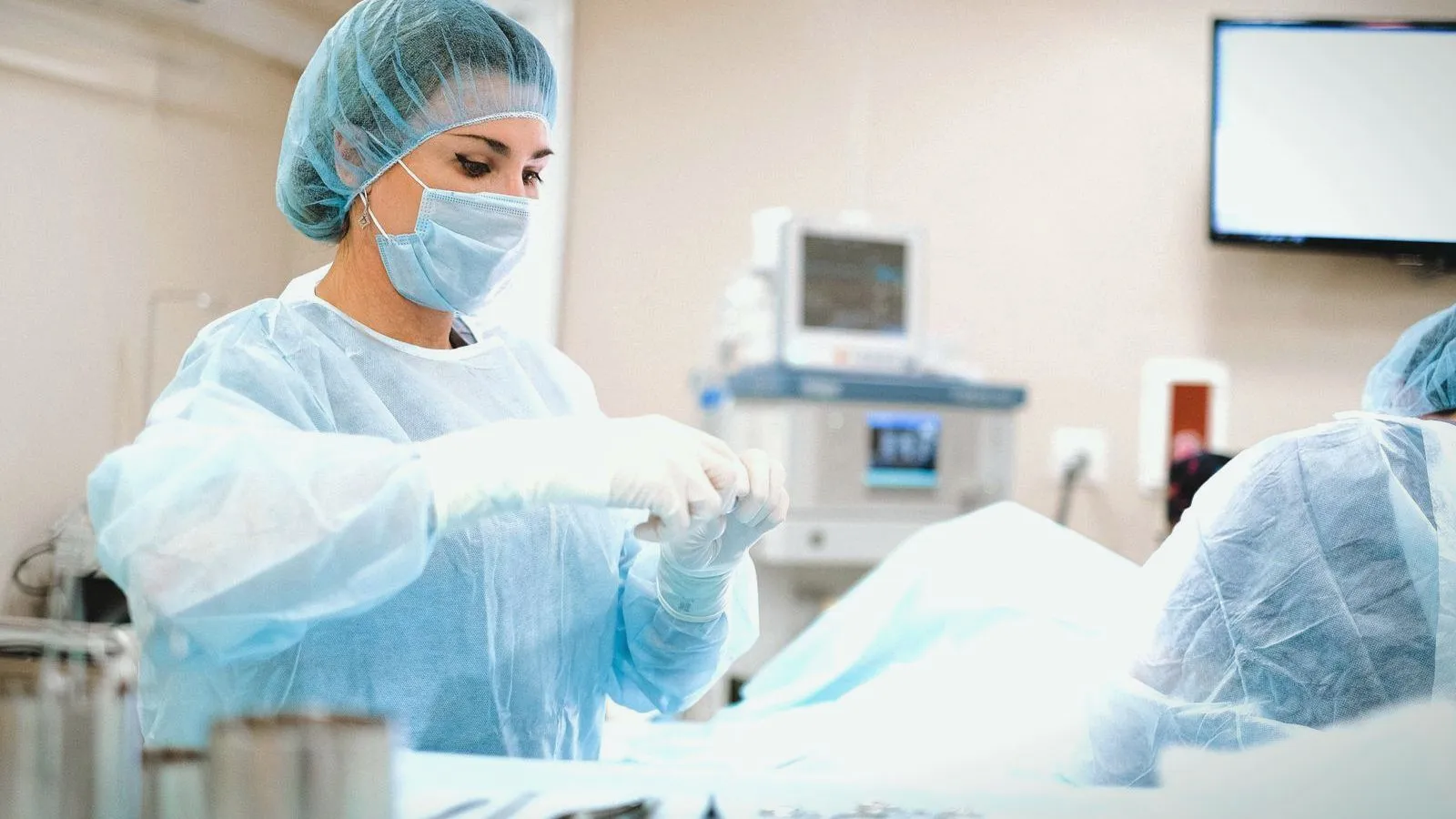A clinician in a surgical cap and gown working beside monitors in a procedure room