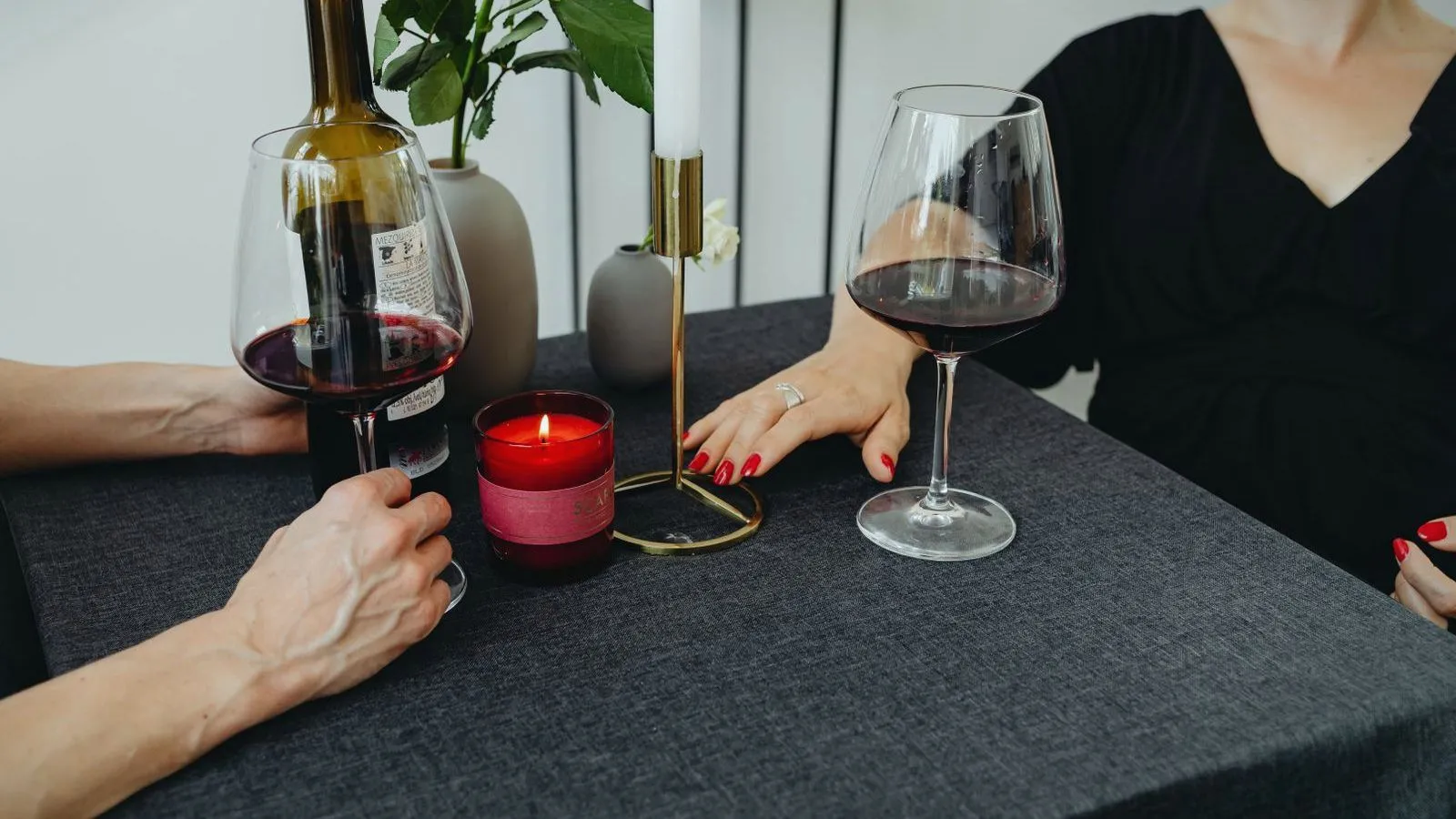 Two women at a dark table with glasses of red wine and a lit candle