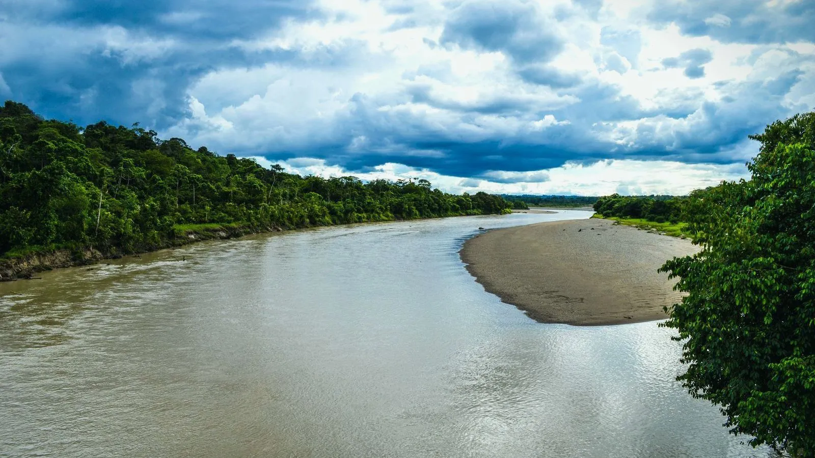 A wide river winding through rainforest under heavy clouds