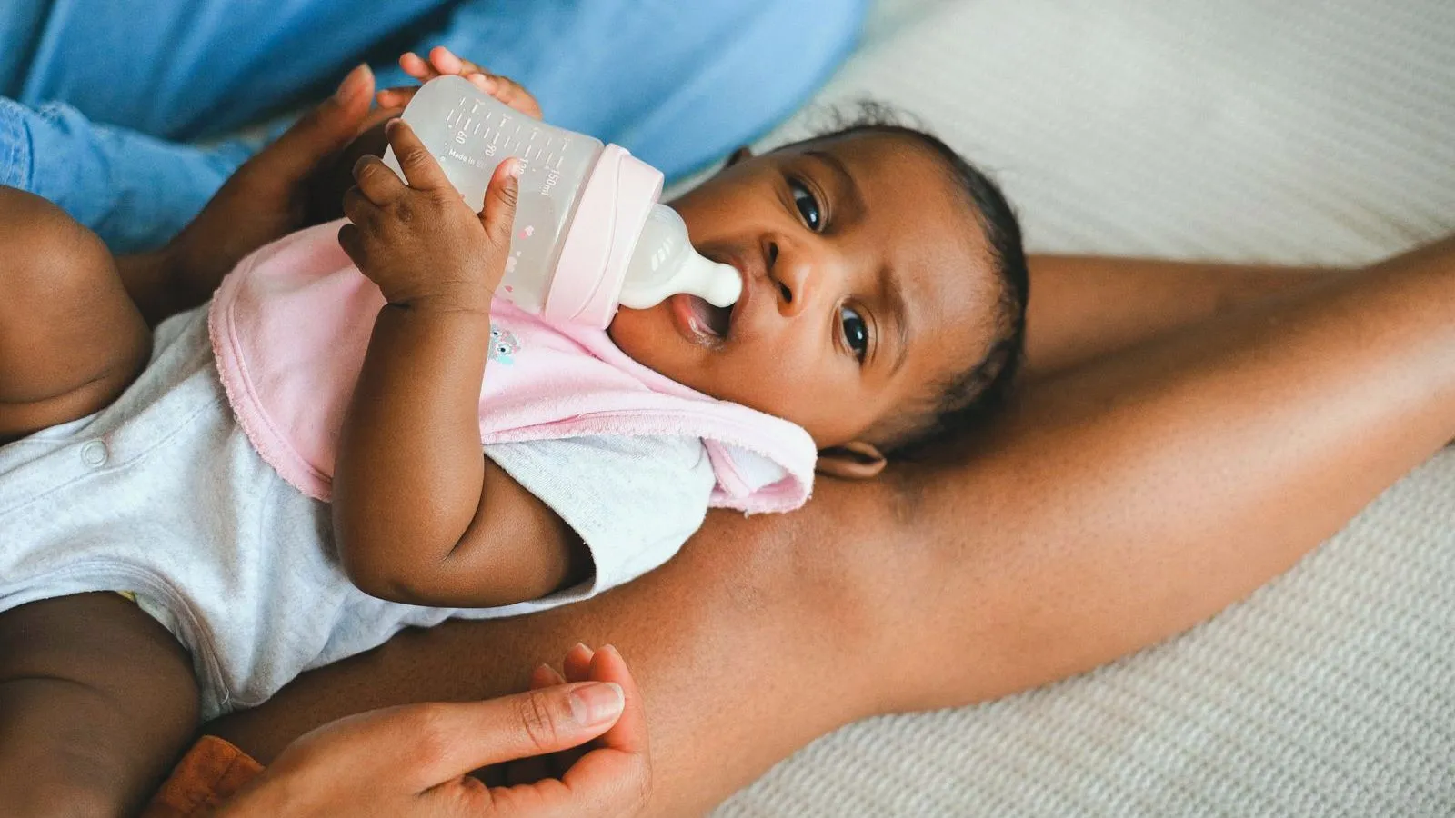 A baby drinking from a bottle held by a parent