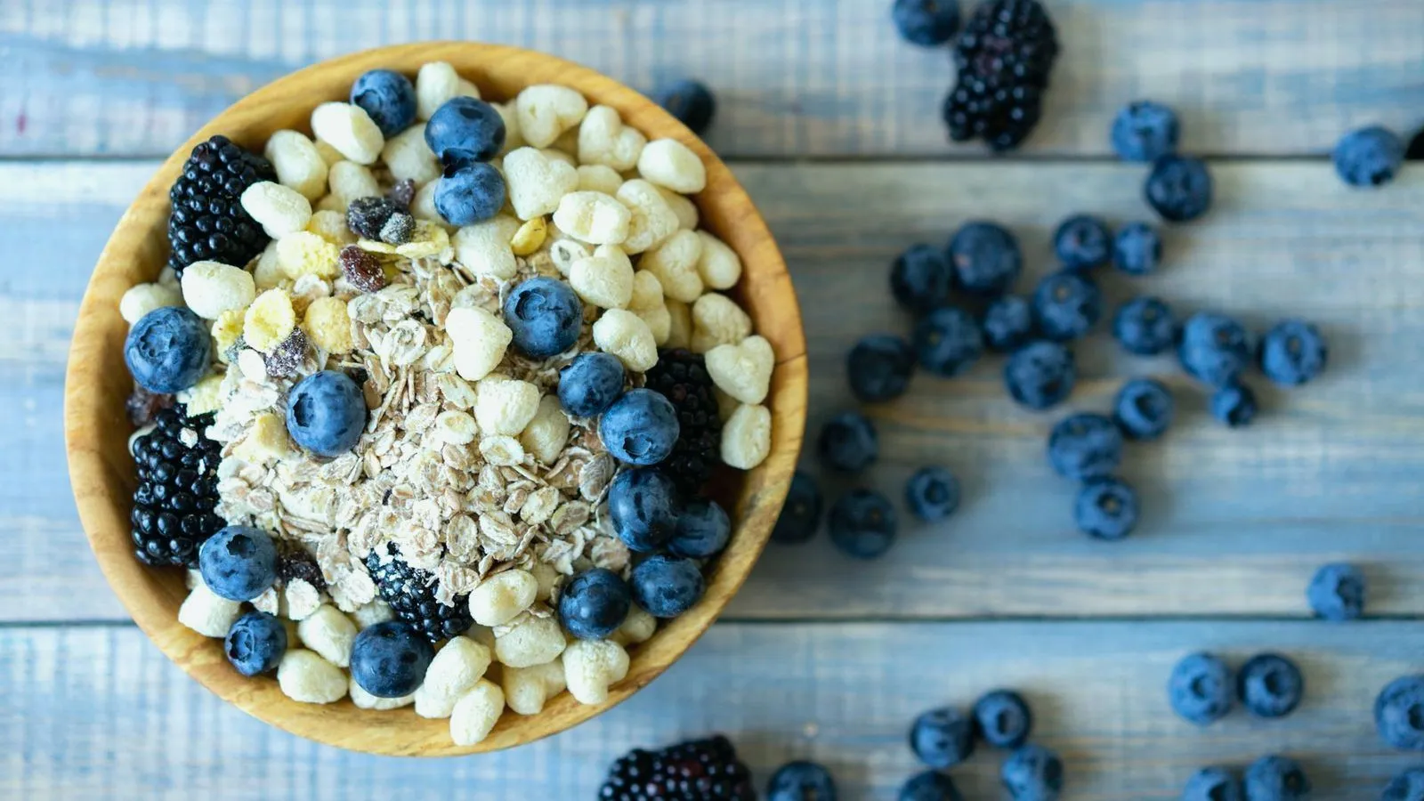 A wooden bowl of oats and puffed cereal topped with blueberries and blackberries