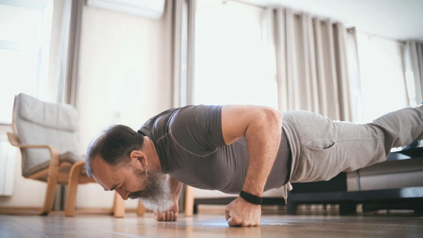 An older man holding a push-up position on the floor of a living room