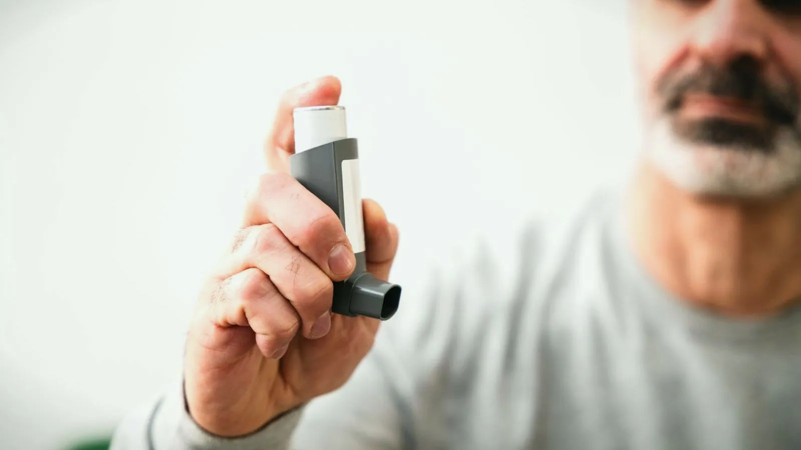 An older man holding an inhaler toward the camera