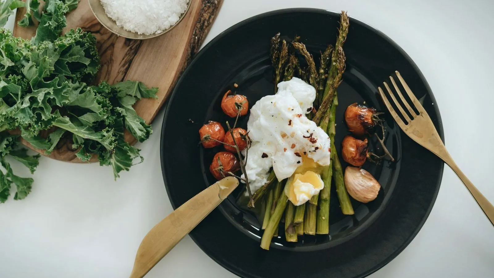 A plate of asparagus, tomatoes and poached egg beside fresh kale