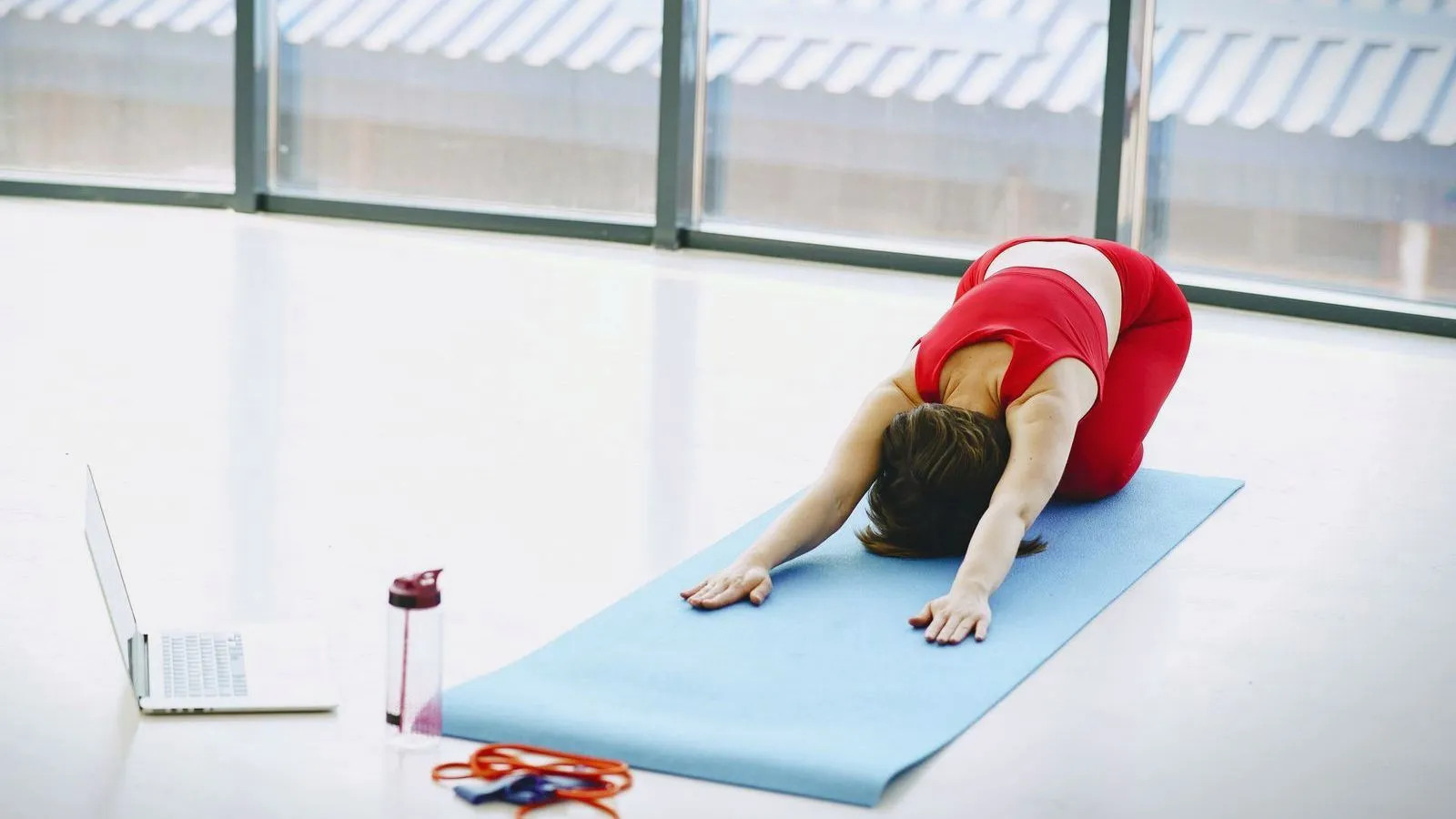 A woman in a red top stretching in a child's pose on a blue exercise mat.