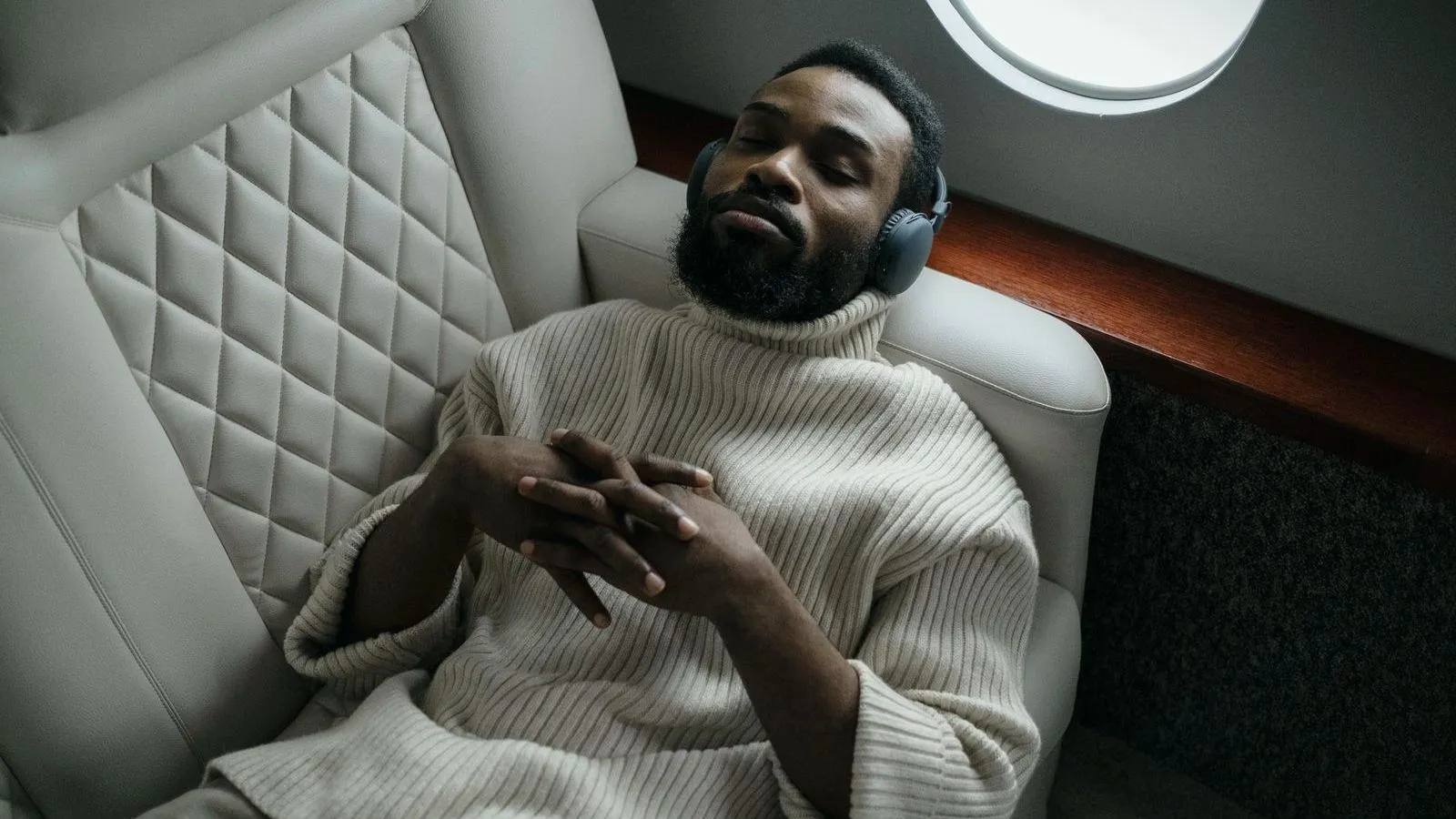 A man reclined in a padded seat with over-ear headphones on and his eyes closed