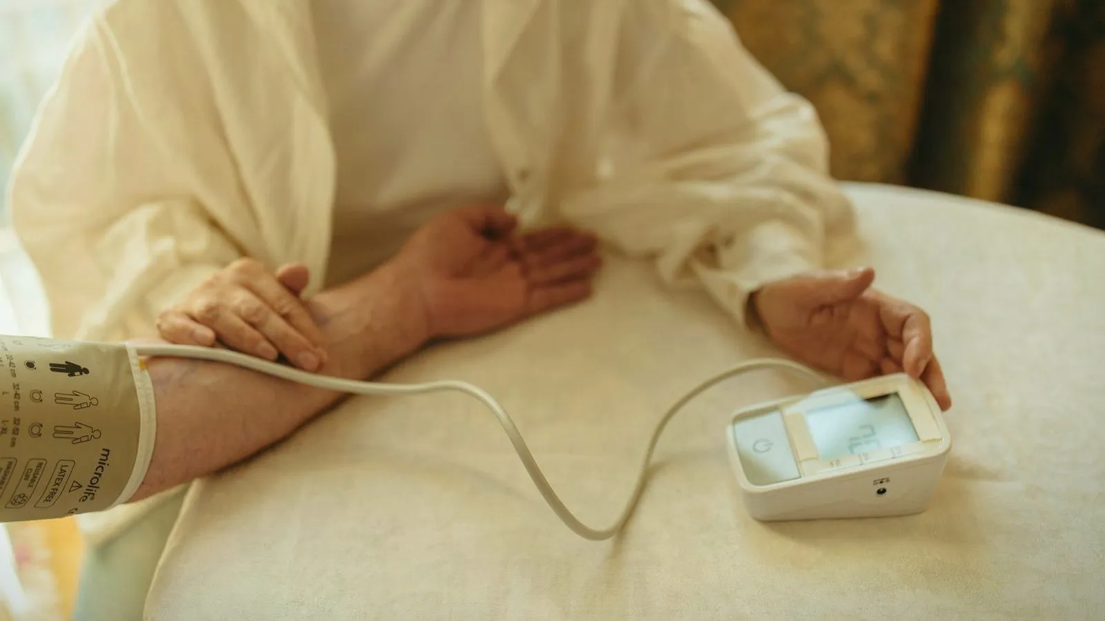 An older person's arm in a blood pressure cuff attached to a home monitor