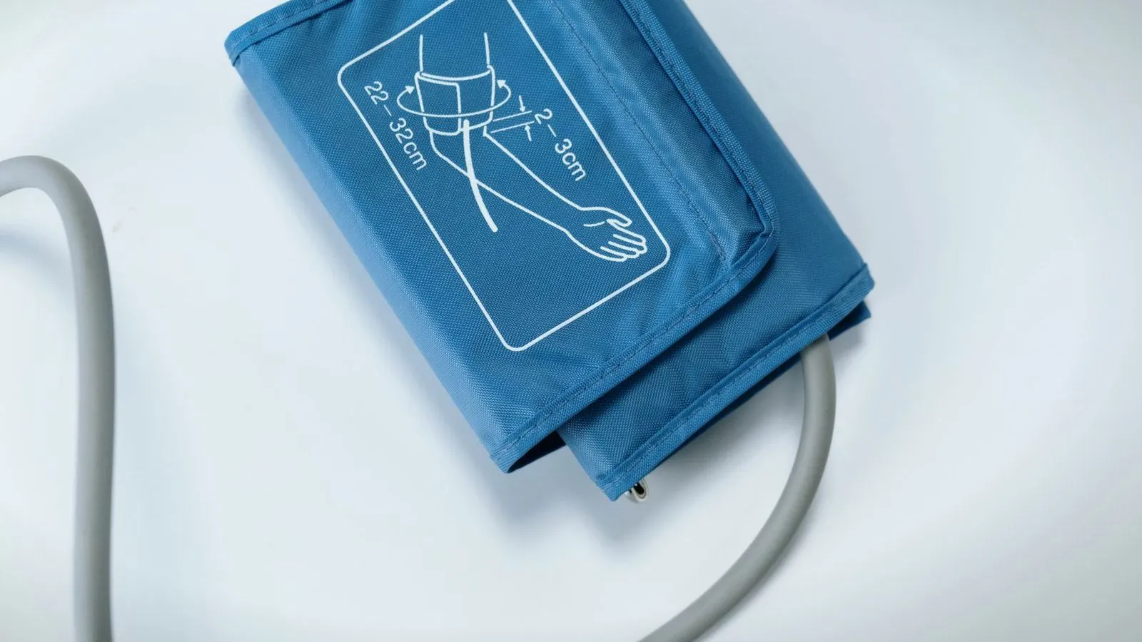 A blue blood pressure cuff and its tubing on a white surface