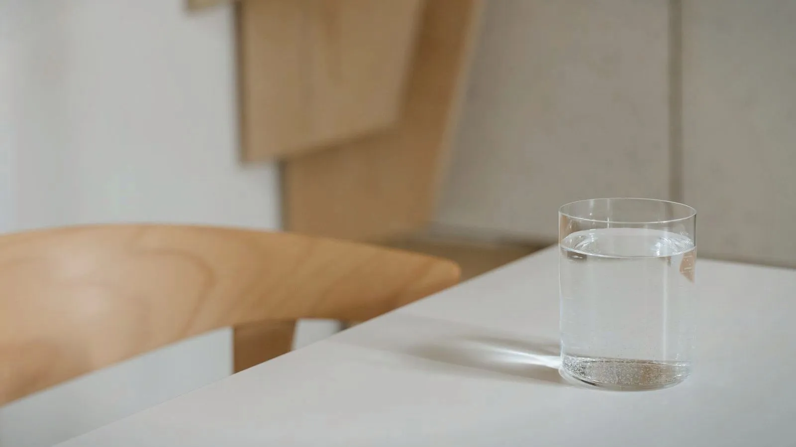 A glass of water on a white table beside a wooden chair