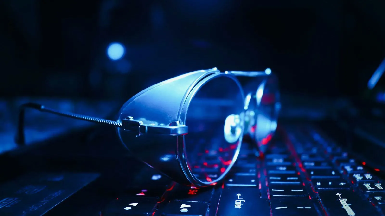 A pair of glasses lying on a keyboard lit in blue.