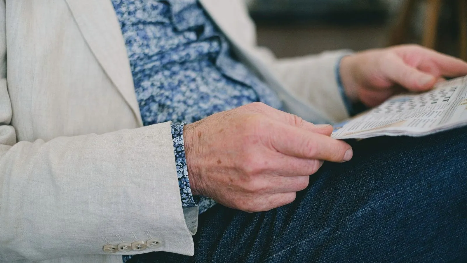 The hands of an older person in a pale linen jacket holding a puzzle page on their lap.