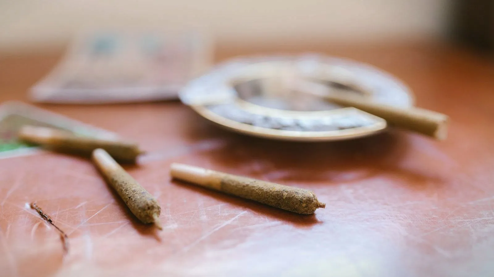 Three hand-rolled joints on a scratched wooden table beside an ashtray