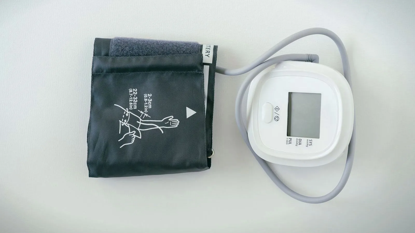 A digital blood pressure monitor and its cuff laid out on a white surface