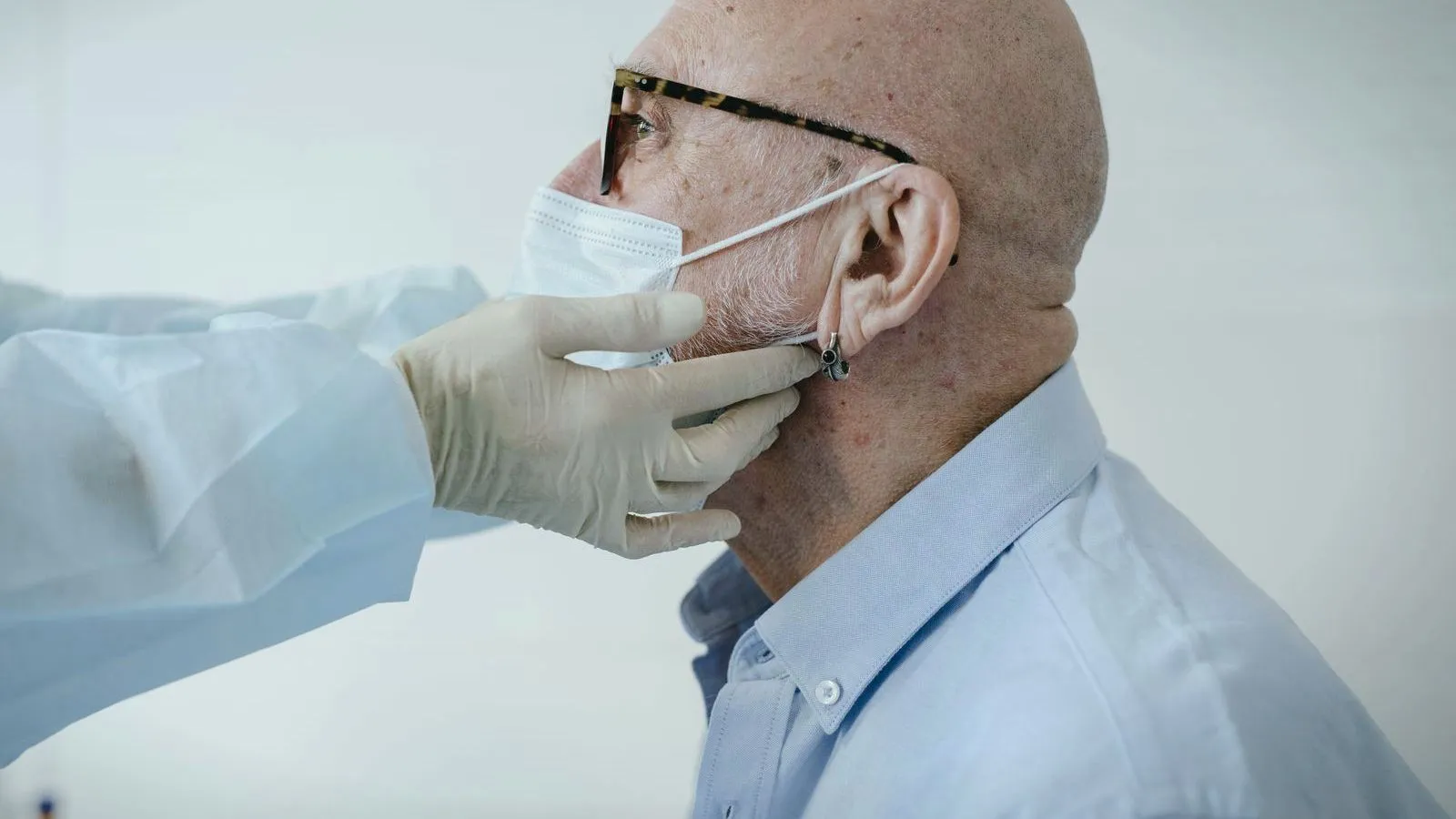 A clinician in gloves examining the neck of an older man who is wearing a face mask.