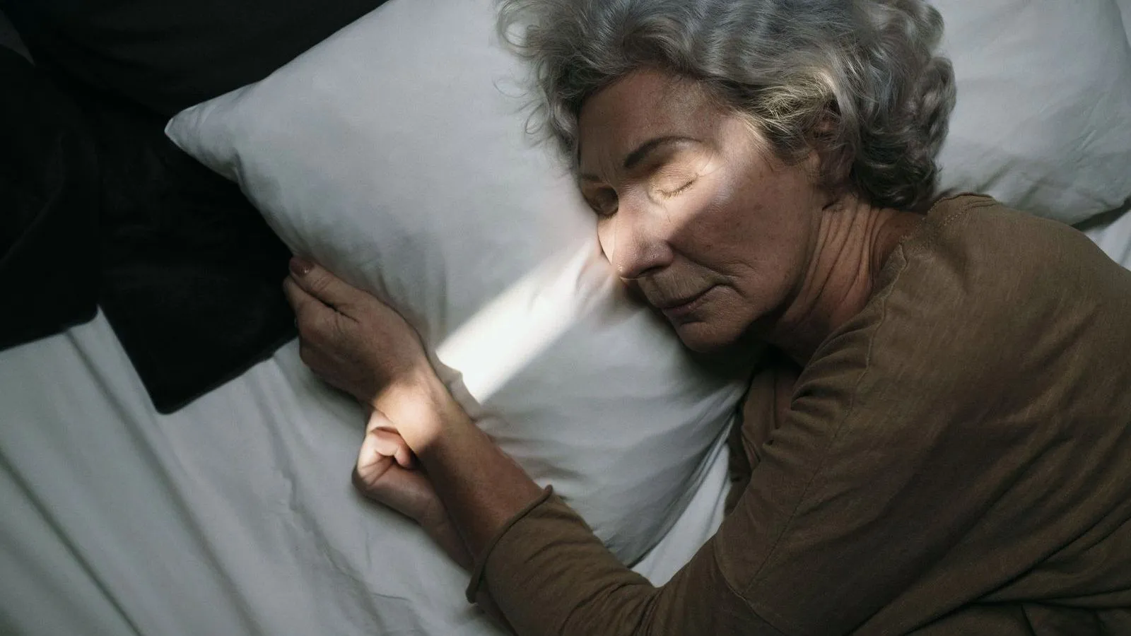 An older woman asleep on a white pillow
