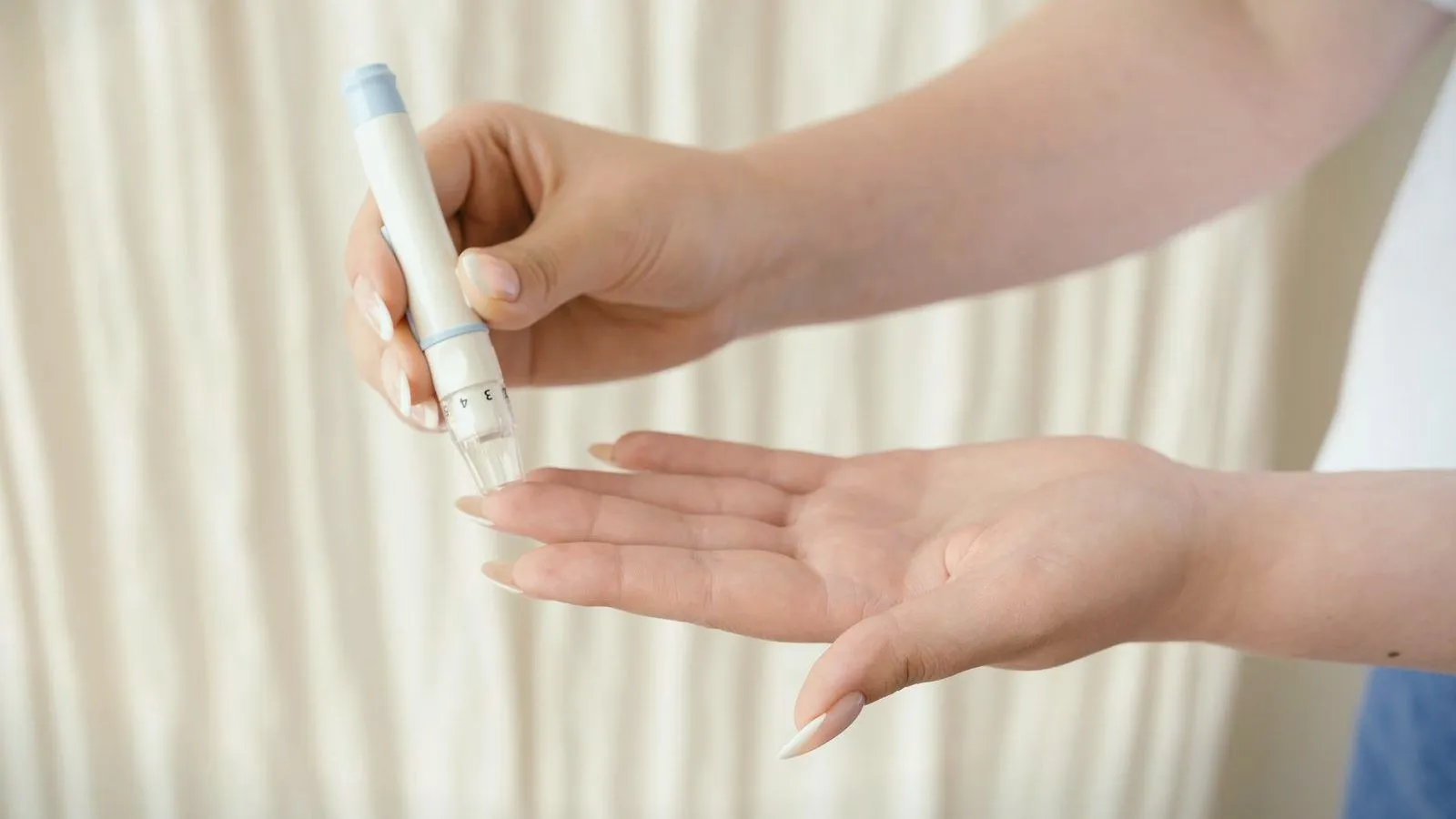 A hand holding a lancing device above an open palm