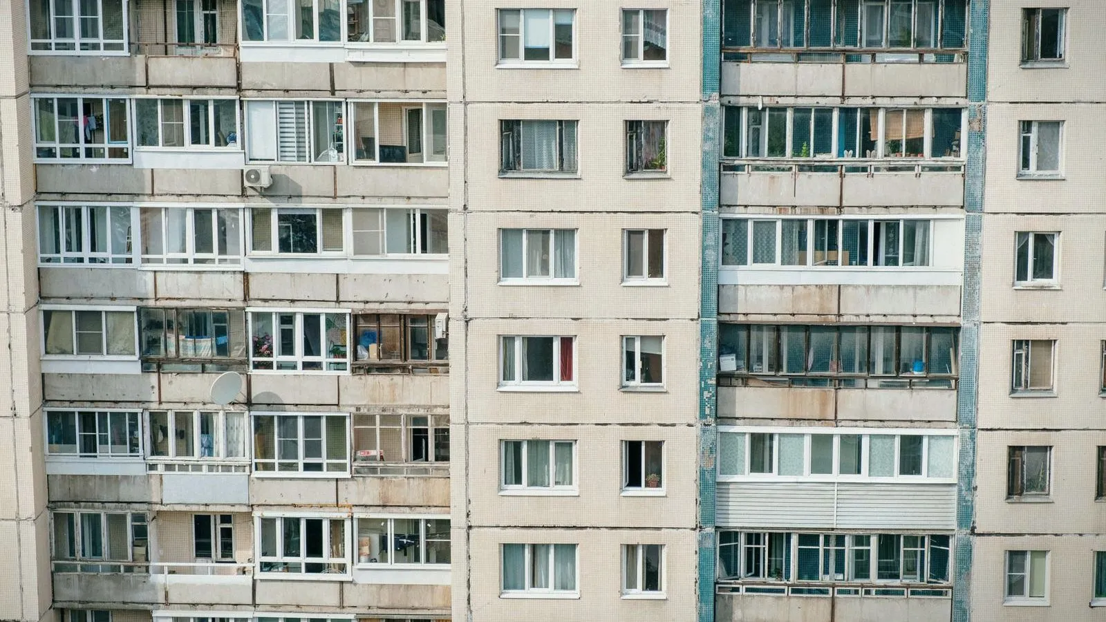 The facade of a concrete apartment block with rows of windows and enclosed balconies.