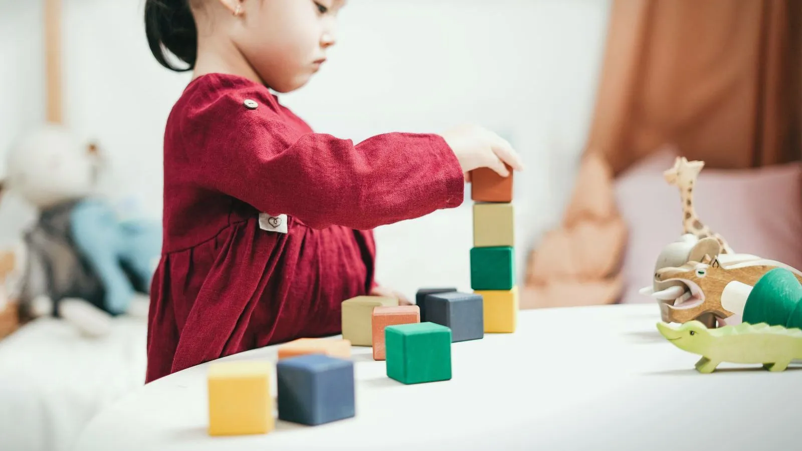 A toddler in a red dress stacking colored wooden blocks