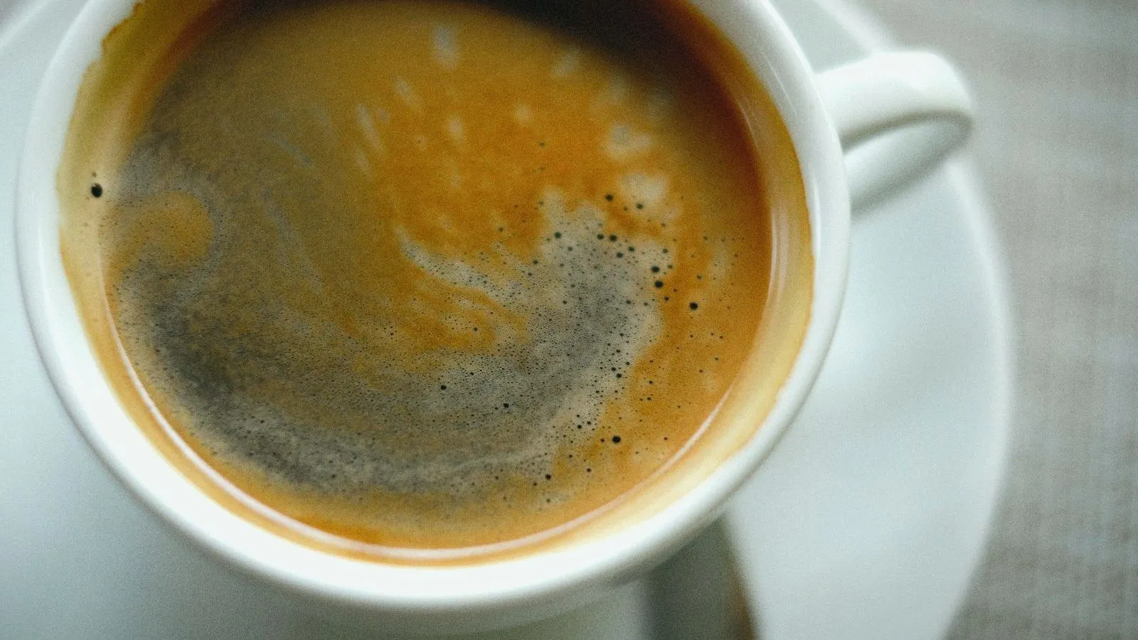 A cup of black coffee on a saucer, seen from above.