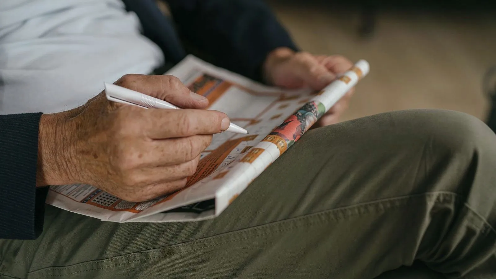 An older person's hands filling in a newspaper puzzle with a pen