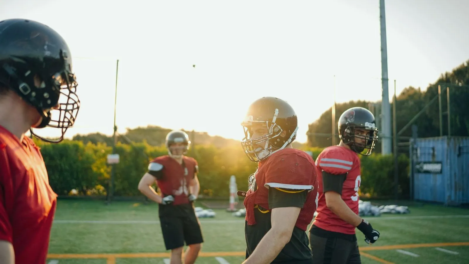 American football players in helmets at practice, backlit by low sun
