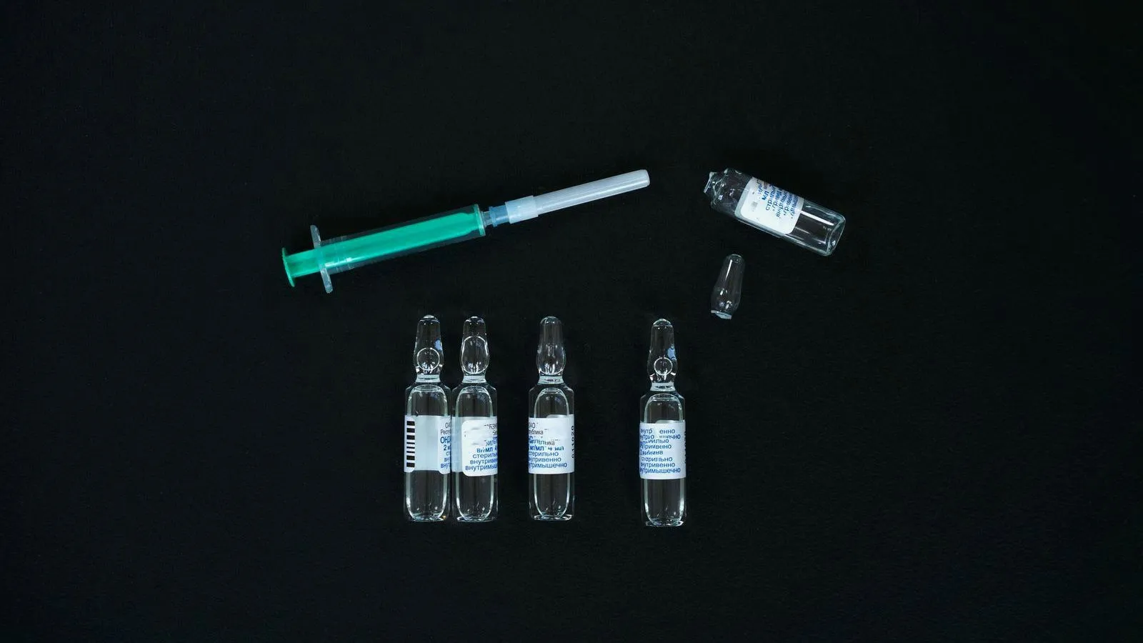 A syringe and four glass ampoules arranged on a black surface