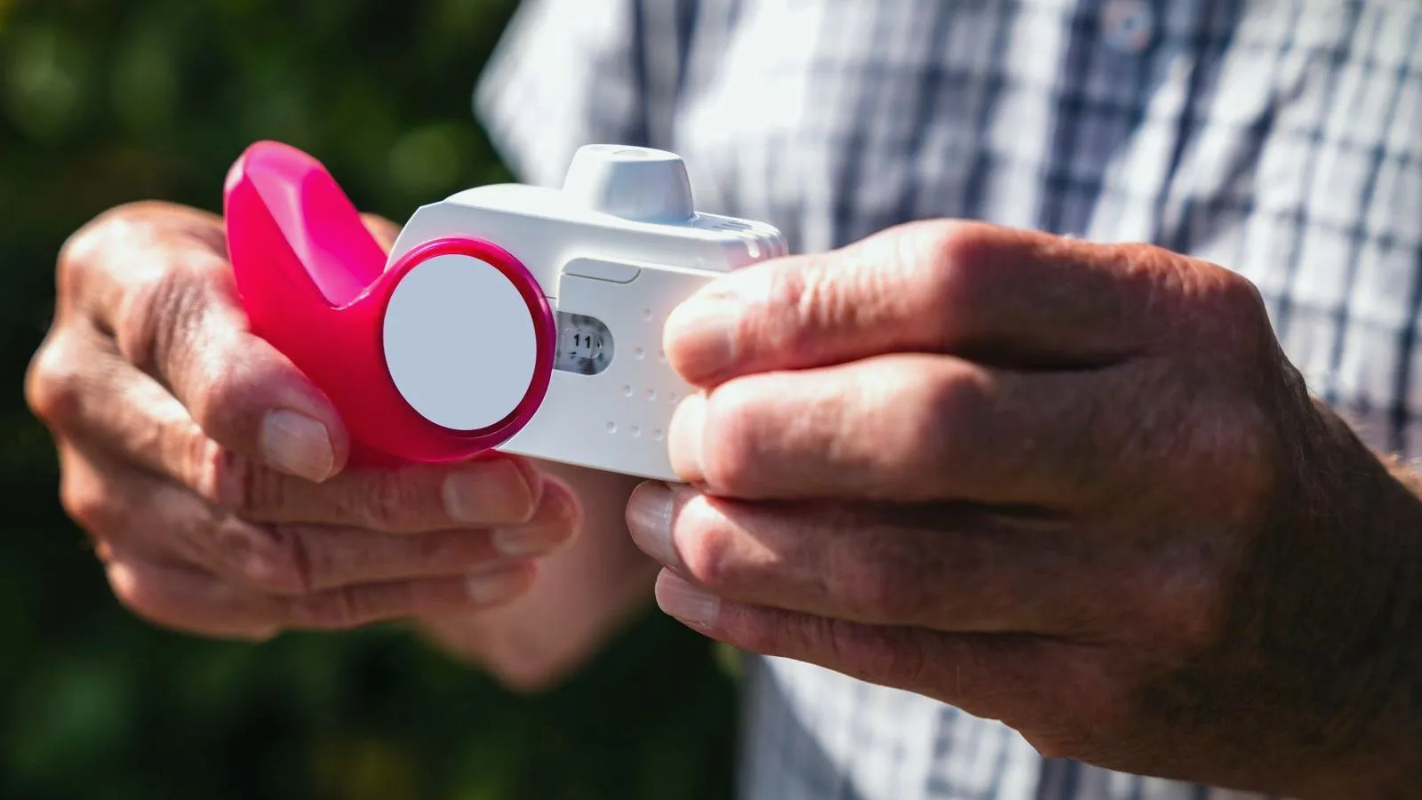 Older hands holding an inhaler and a spacer outdoors