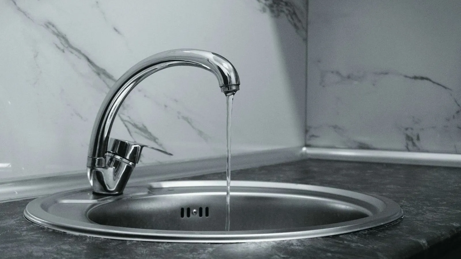 Water running from a chrome kitchen tap into a round steel sink