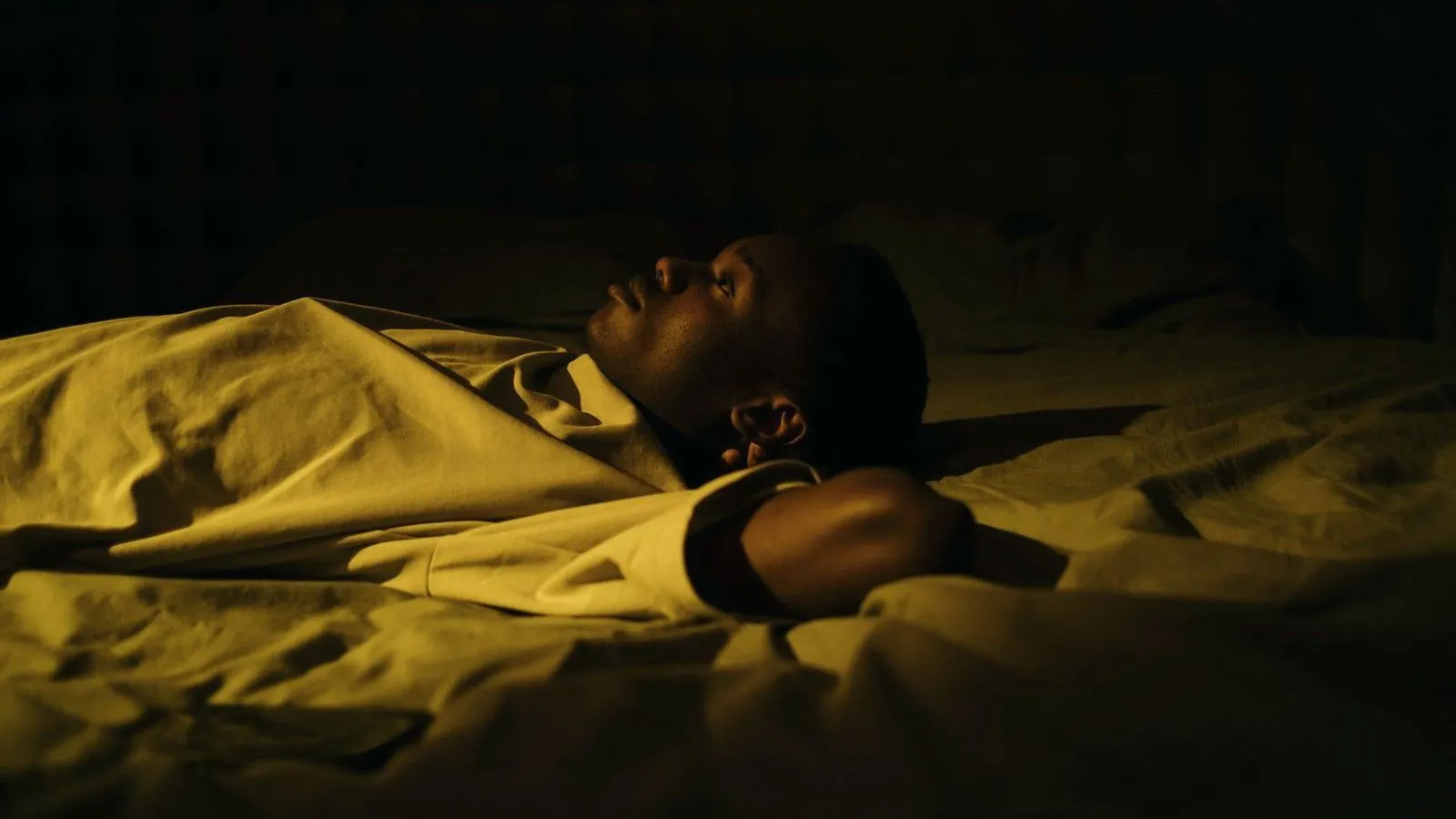 A person lying awake on their back in a dimly lit bedroom