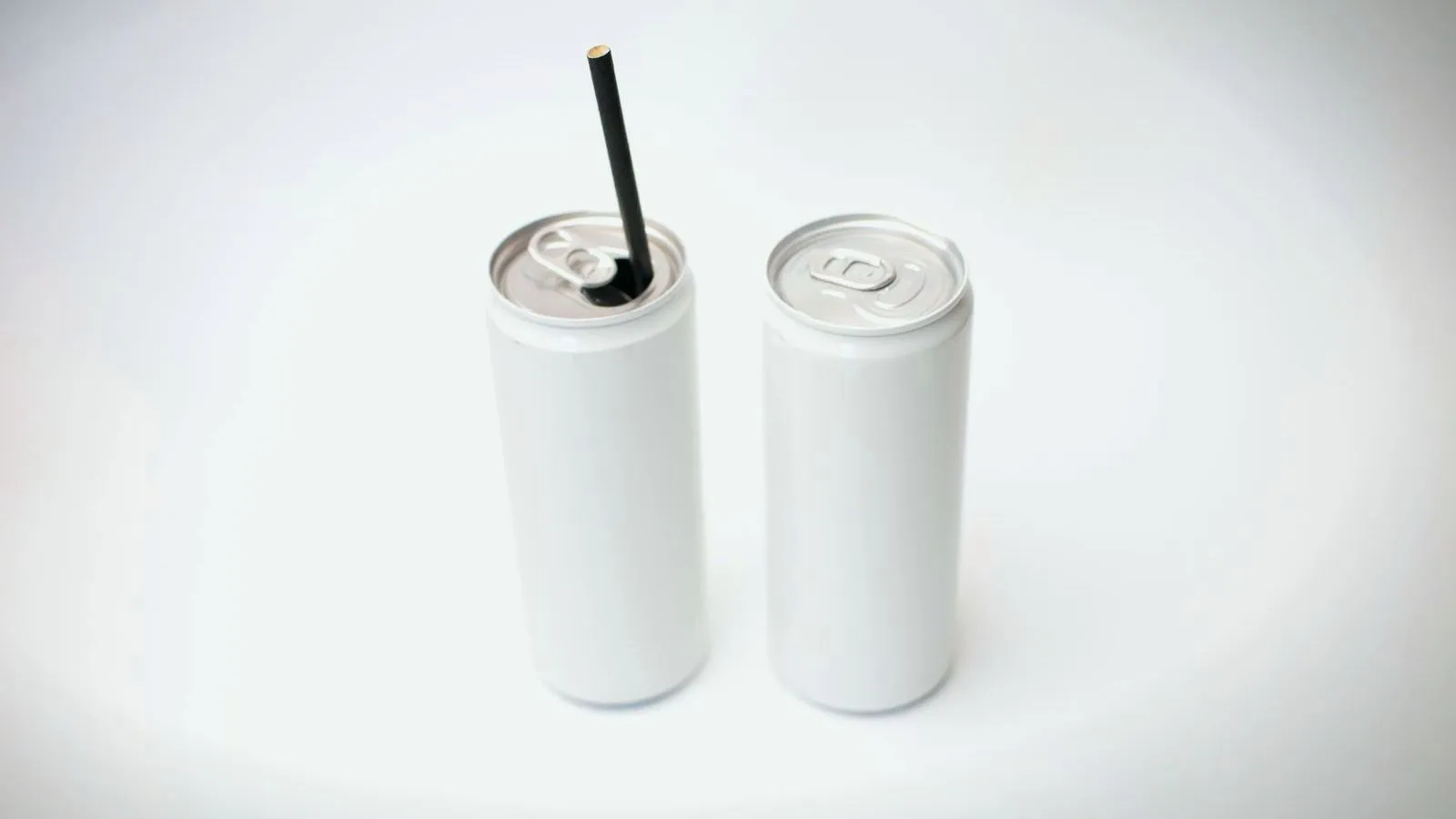 Two plain white drink cans on a white surface, one opened with a black straw in it.