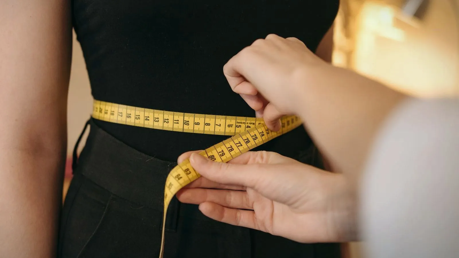 A tape measure being drawn around a waist over dark clothing