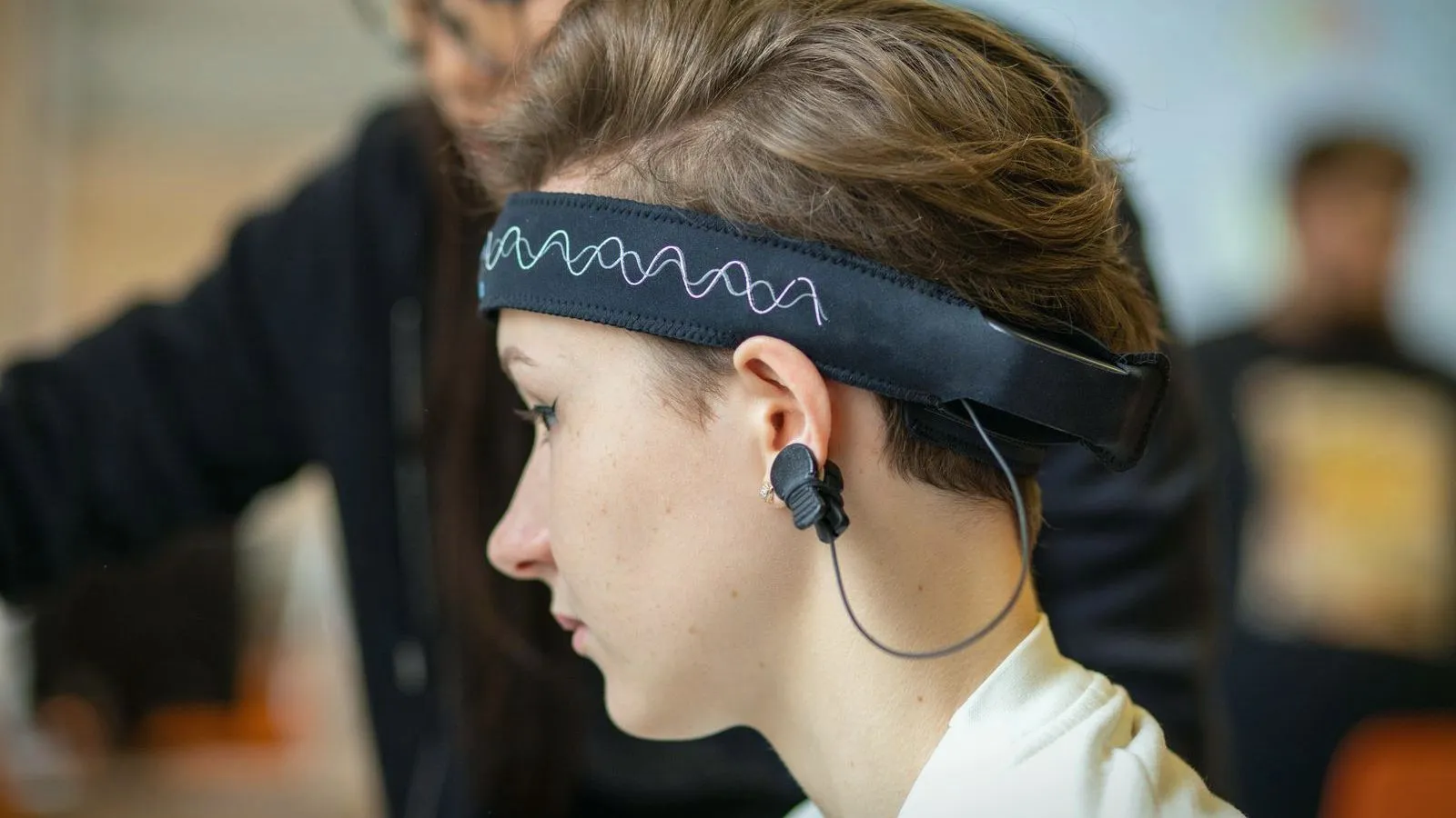 A woman in profile wearing an EEG headband with a sensor clipped to her ear.