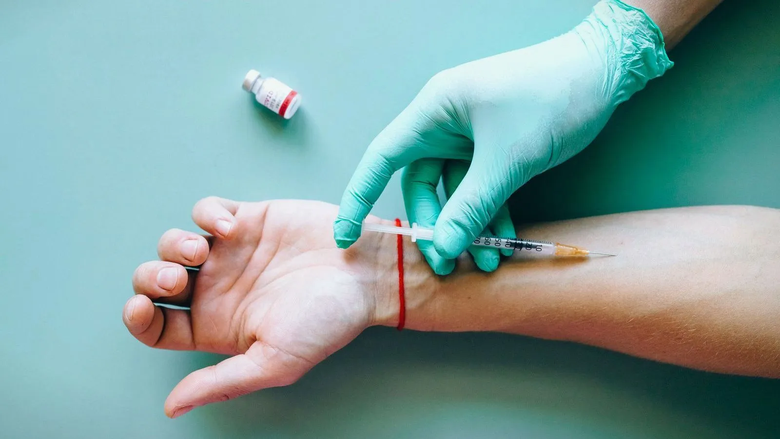 A gloved clinician taking blood from a person's inner wrist