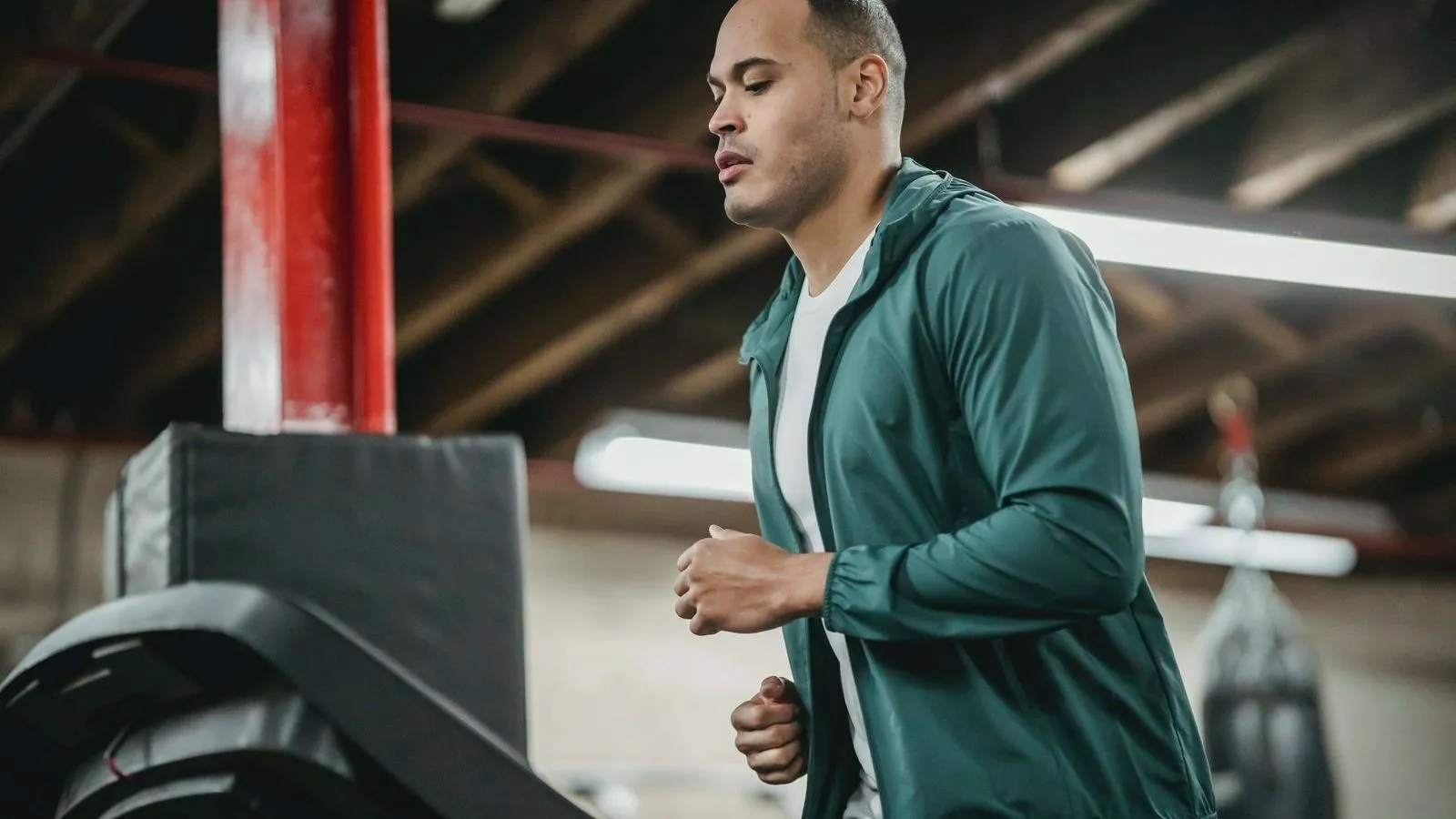 A man in a green zip-up jacket running on a treadmill in a gym