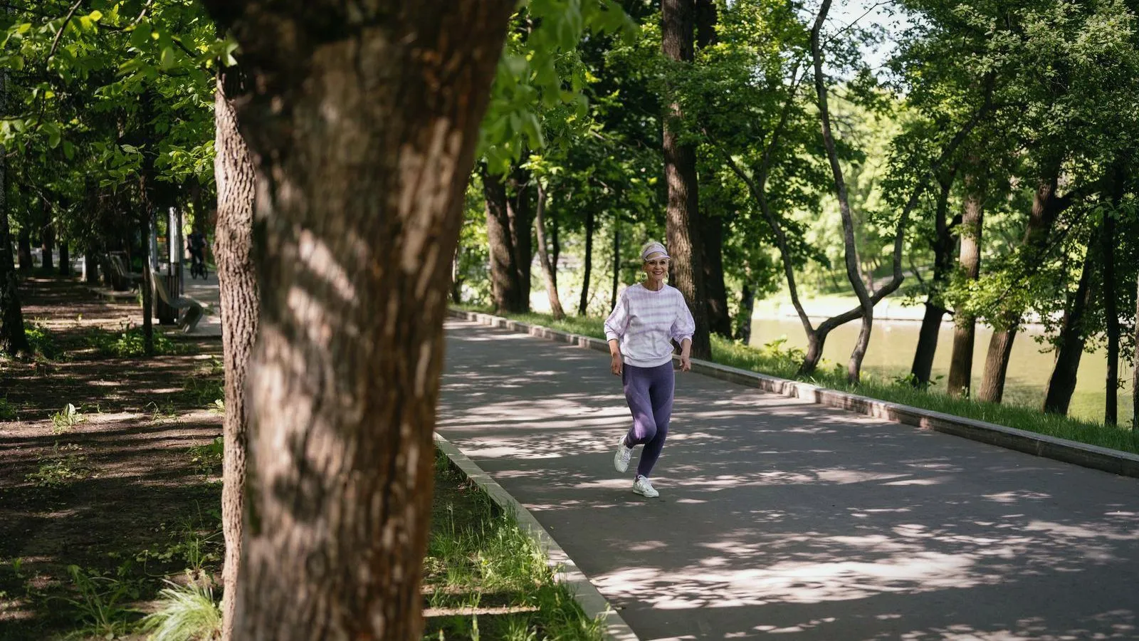 An older woman jogging along a tree-lined park path on a sunny day
