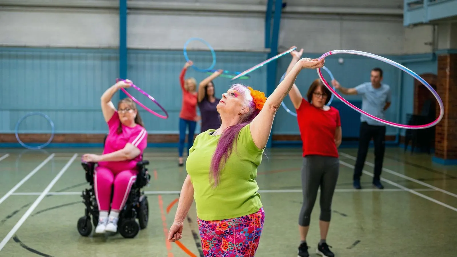 Older adults exercising with hoops in a gym, one of them in a wheelchair.