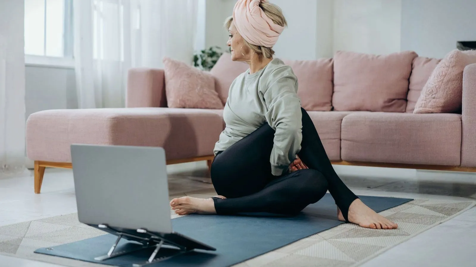 An older woman stretching on a mat at home in front of a laptop