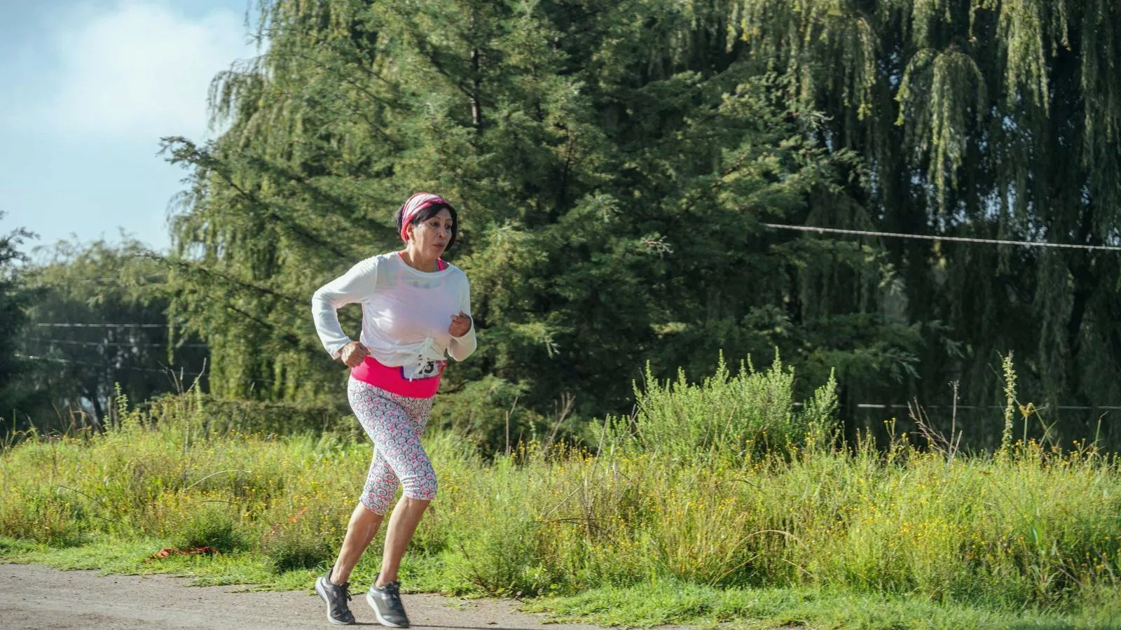 A woman running along a path beside long grass and willow trees
