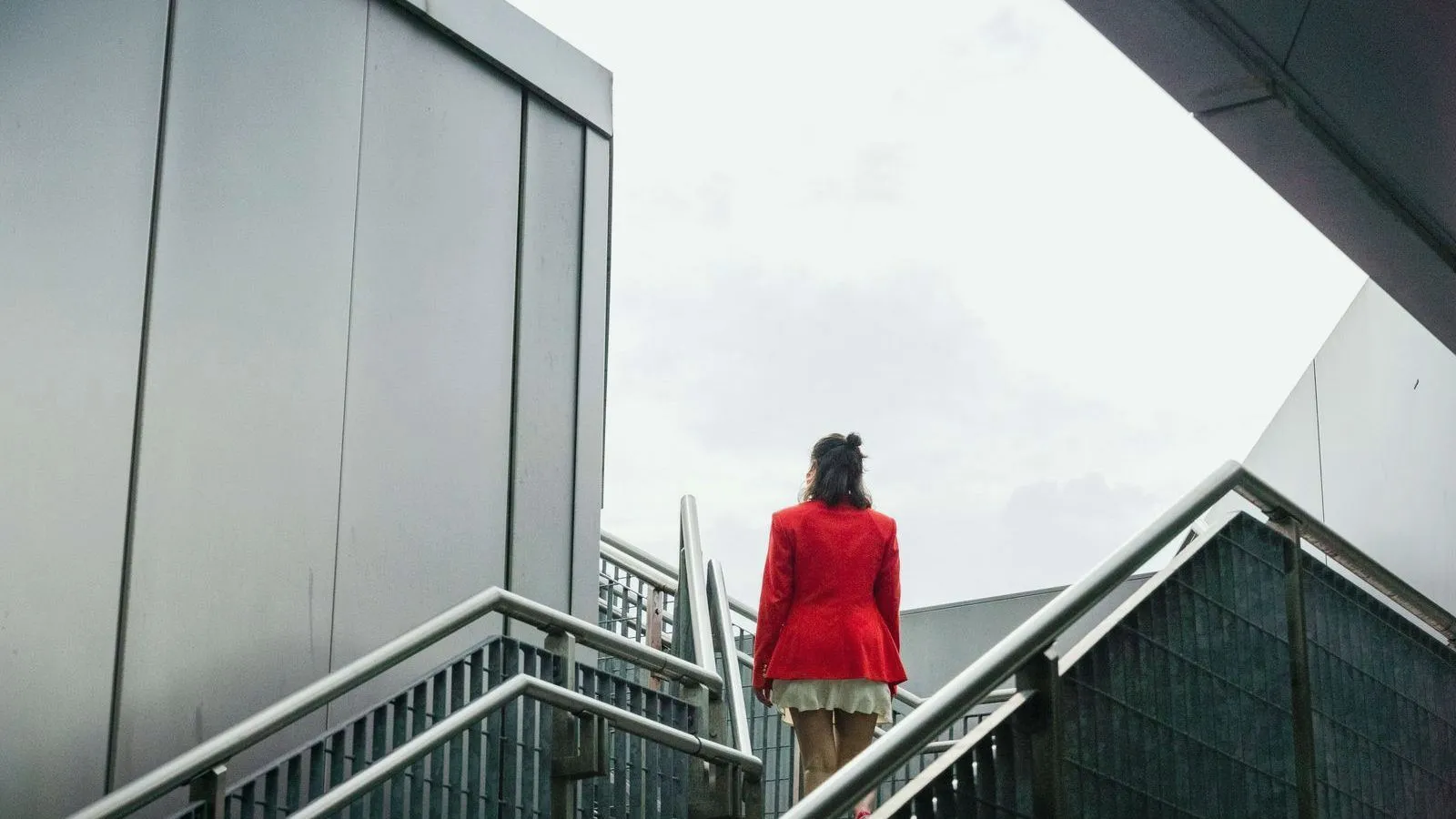 A woman in a red coat climbing an outdoor staircase, seen from behind
