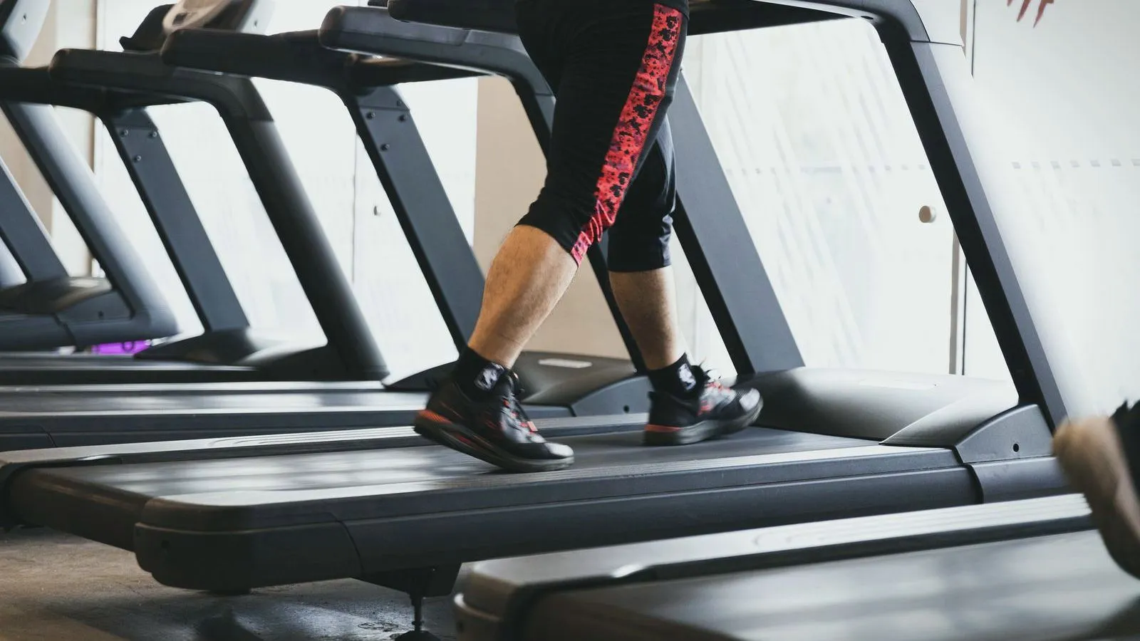 The legs of a person walking on a treadmill in a row of gym machines.