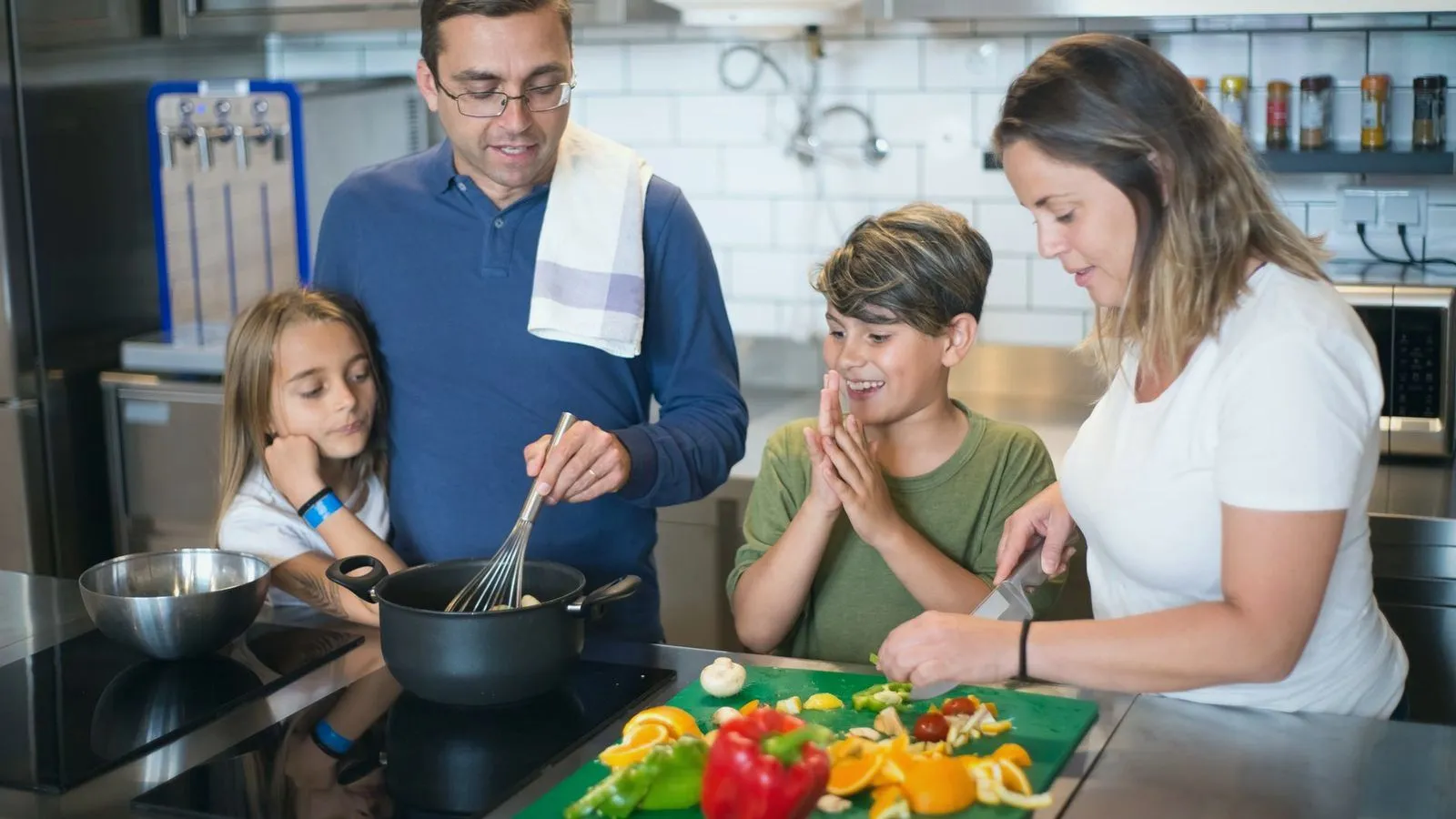 Two parents and two children preparing vegetables together at a kitchen counter
