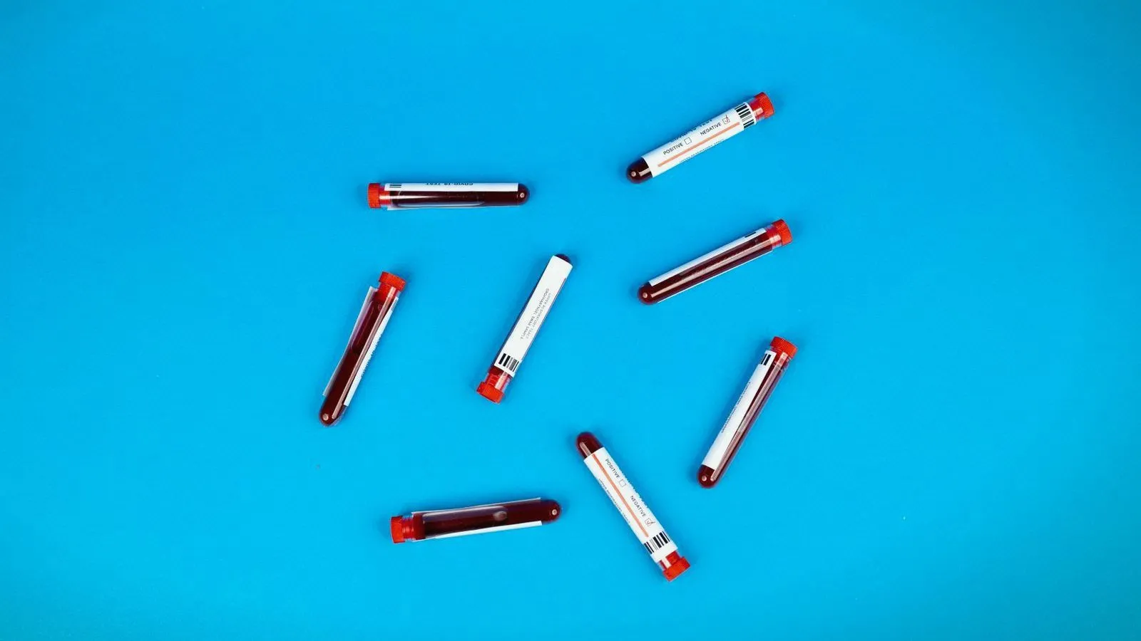 Blood sample tubes with red caps scattered across a bright blue surface.