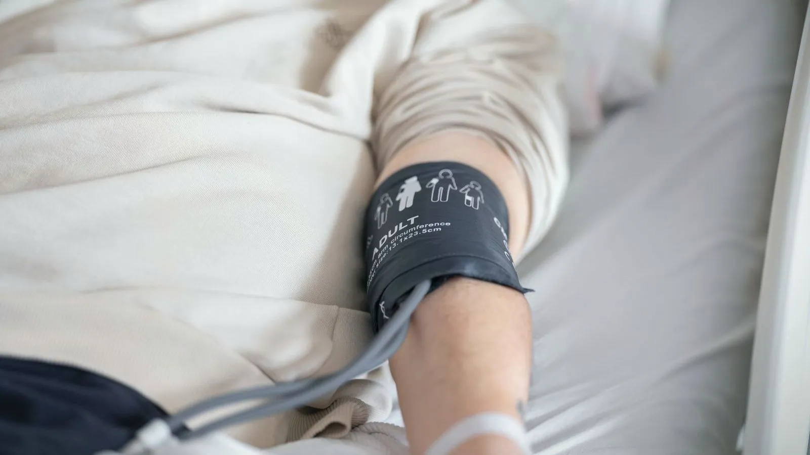A blood pressure cuff fastened around the arm of a patient lying in a hospital bed