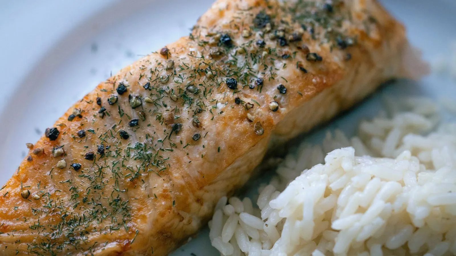 A herb-topped salmon fillet on a plate beside a portion of white rice