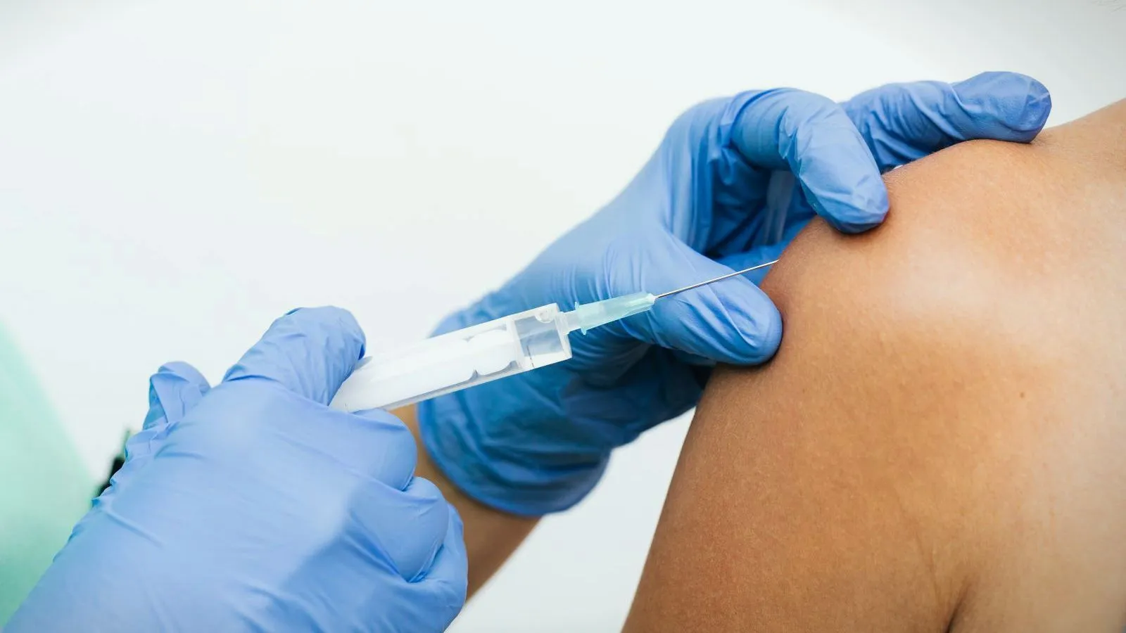 Gloved hands giving an injection into a person's upper arm