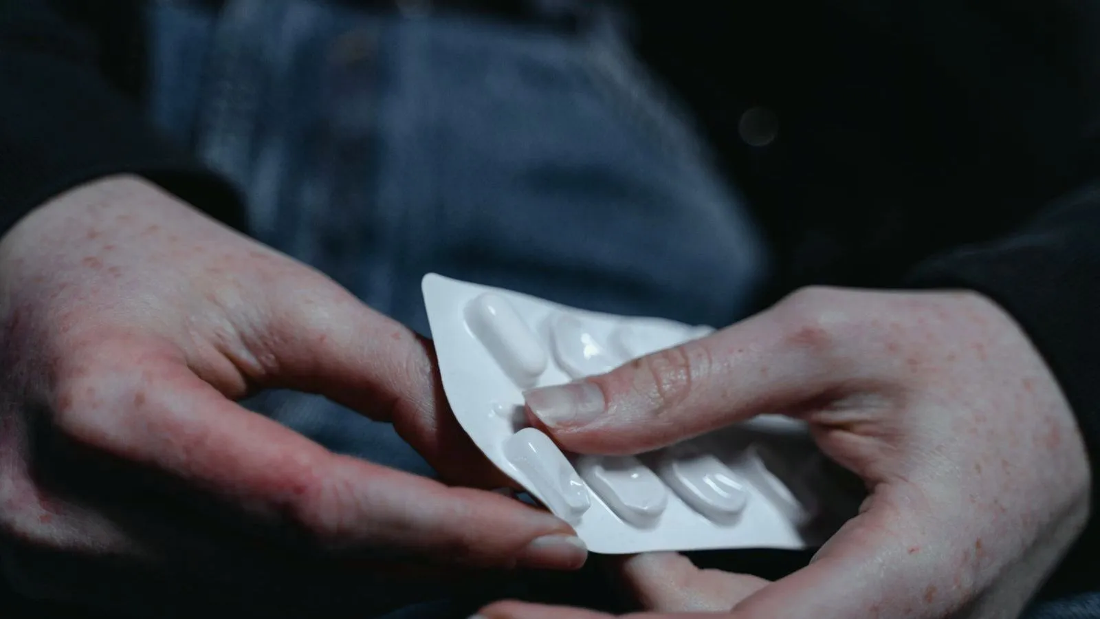 Hands holding a blister pack of white capsules against dark clothing.
