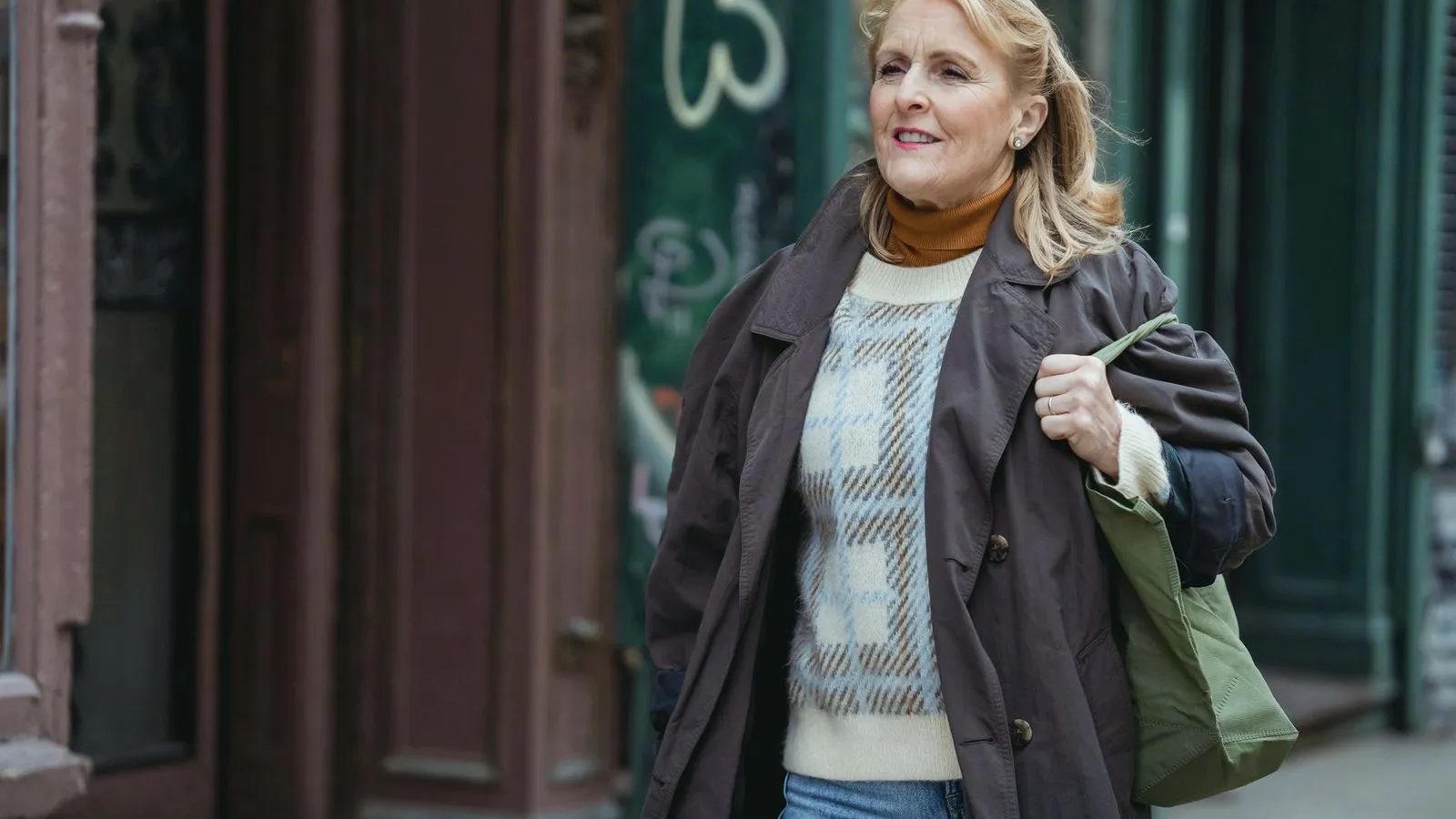 A middle-aged woman in a coat walking past shopfronts