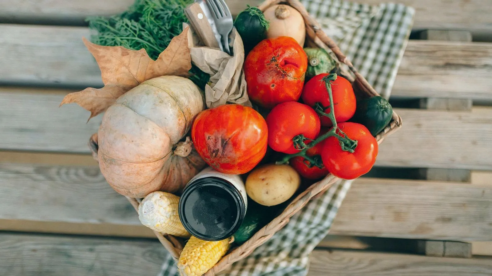A wicker basket of tomatoes, squash and mixed vegetables on a checked cloth