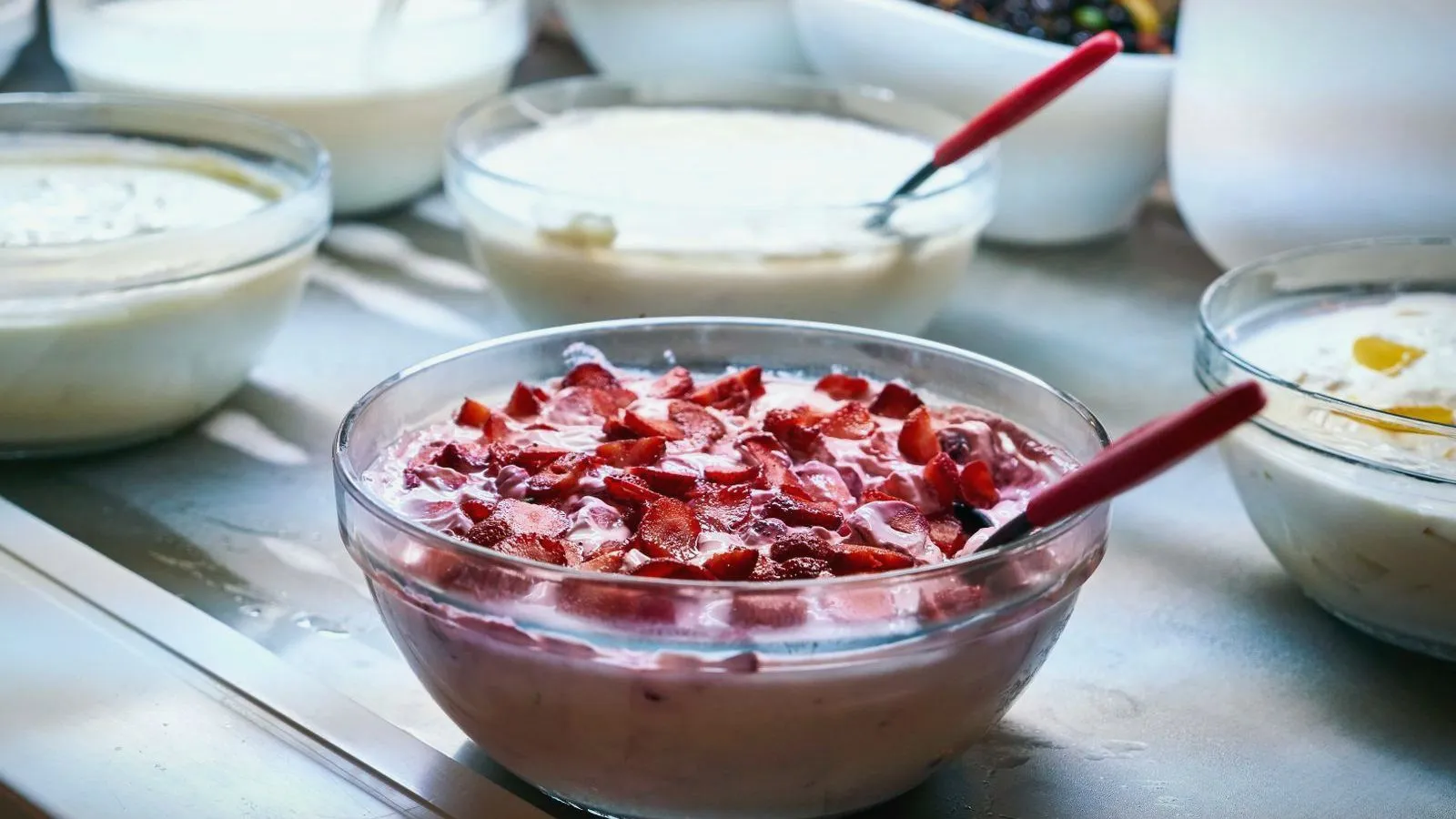 Glass bowls of yogurt on a table, one mixed with chopped strawberries.